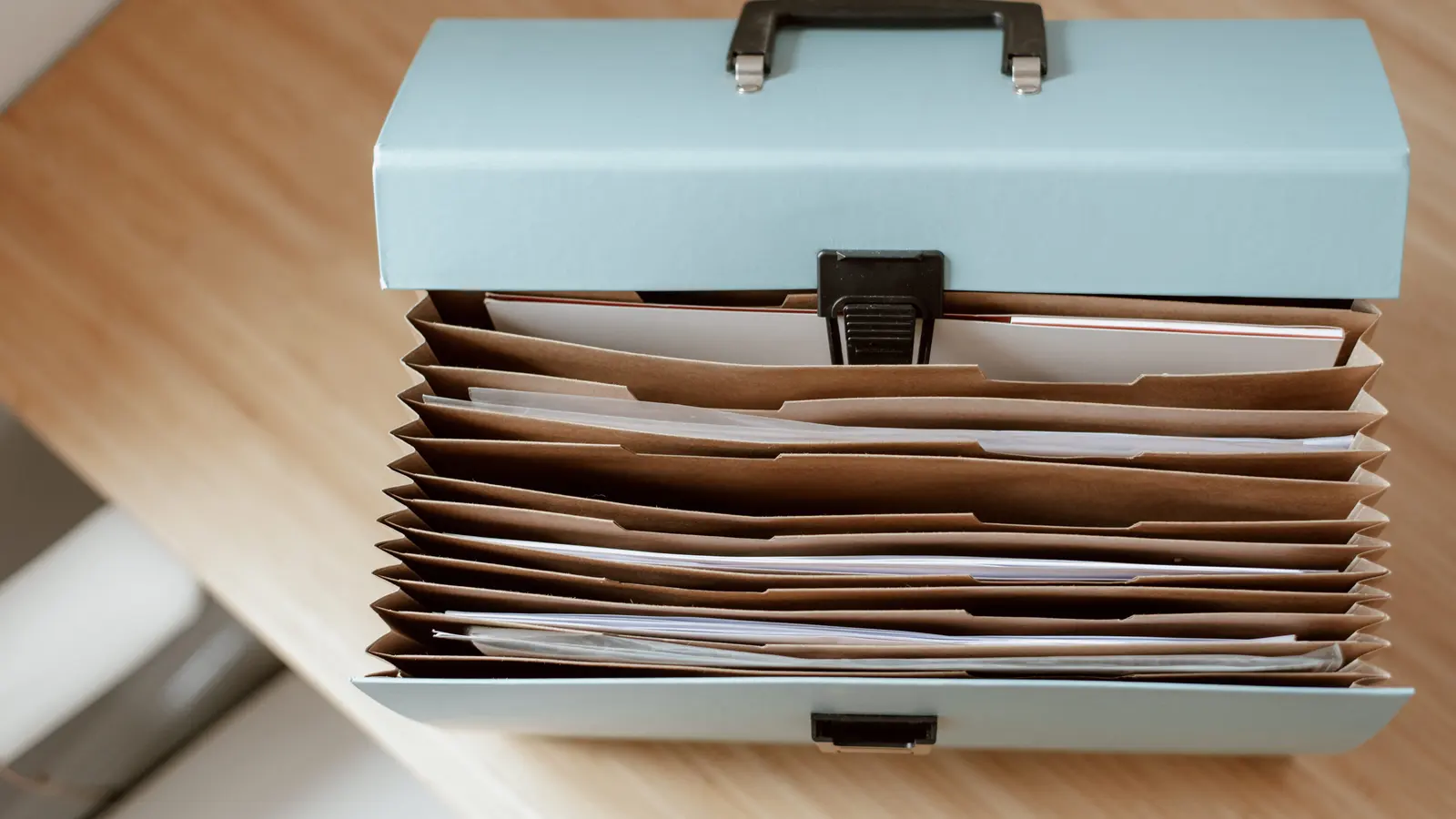 An expanding cardboard document wallet, open and full of papers, standing on a light wooden table