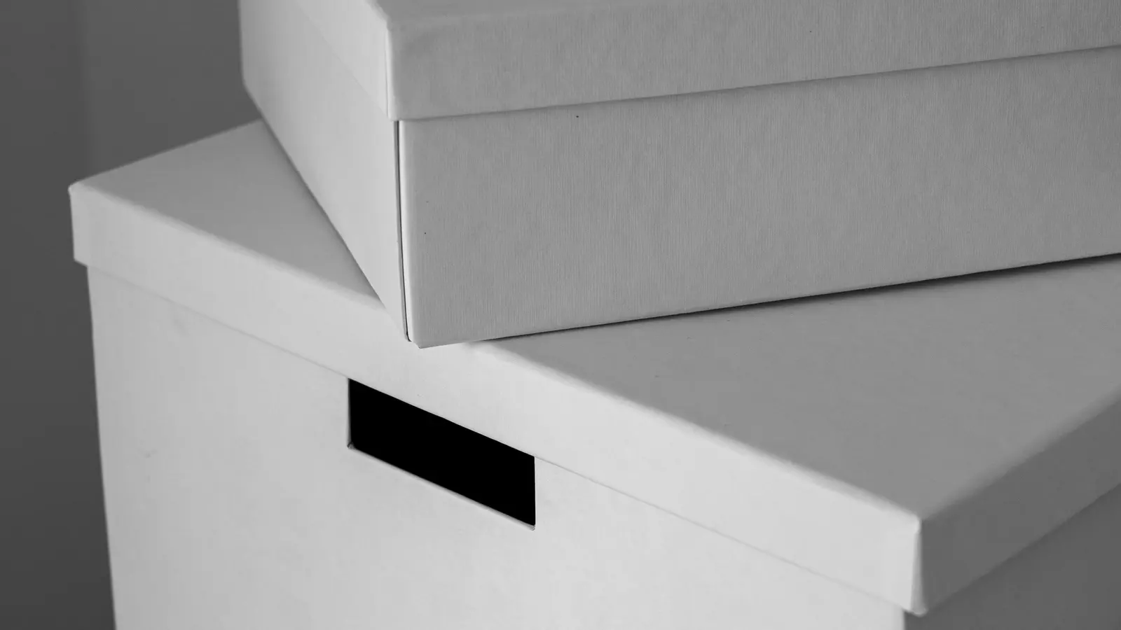 Two plain white archive boxes stacked one on the other against a bare grey wall.